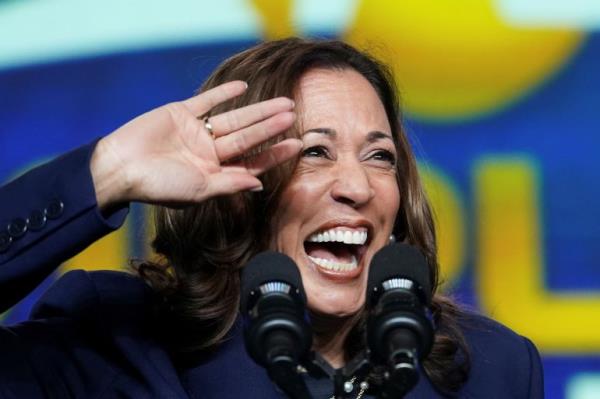 US Vice President and likely Democratic nominee Kamala Harris smiles and holds her hand up at a microphone